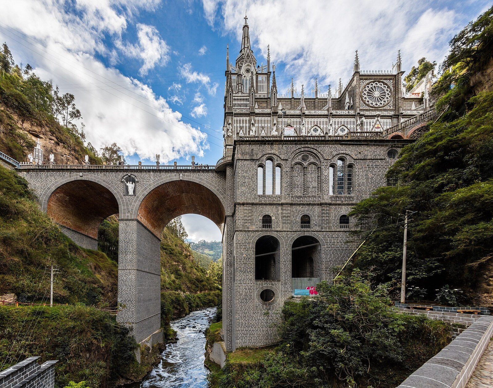 Mặt tiền đền thánh Las Lajas nhìn từ dưới hẻm núi, với cây cầu hai vòm bắc qua sông Guáitara